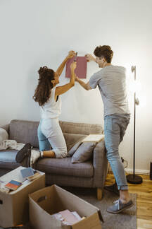 couple helping each other while mounting photo frame on wall at home MASF34960