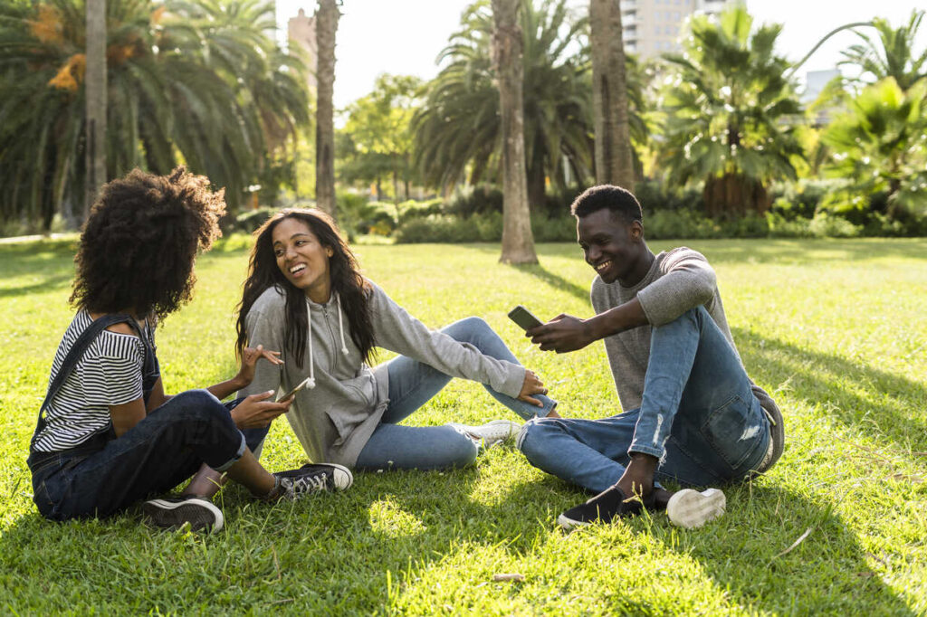 friends sitting on grass having fun using smartphone GIOF05406